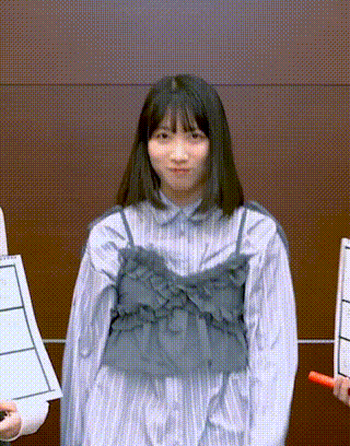 a girl in a striped dress is standing in front of a brown wall holding a red stick .