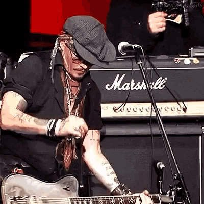 a man wearing a hat is playing a guitar in front of a marshall amplifier .