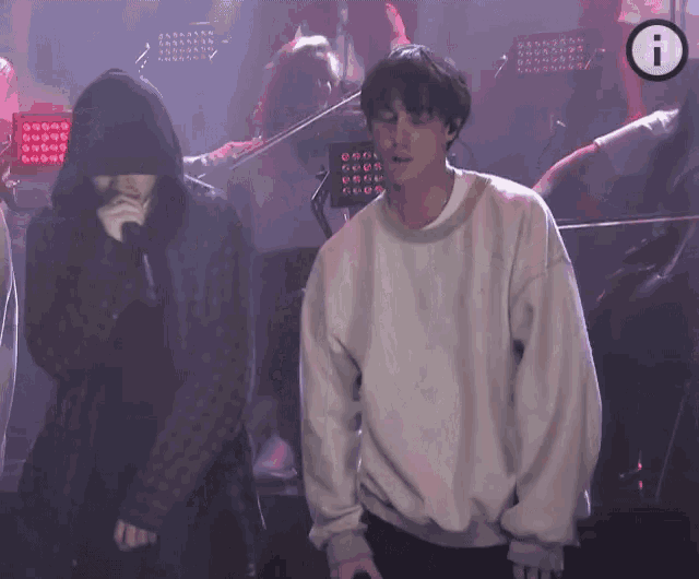 a man in a hoodie is standing next to another man in a white sweater