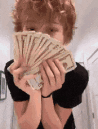 a young man is holding a bunch of money in front of his face .