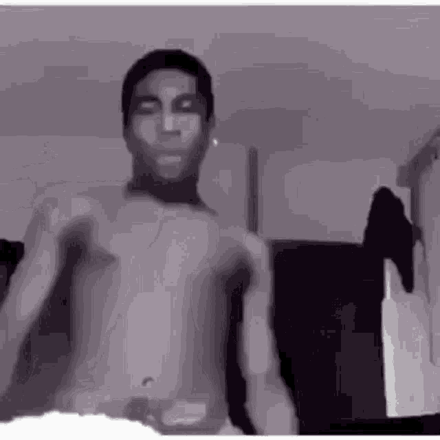 a man without a shirt is dancing in a room in a black and white photo .