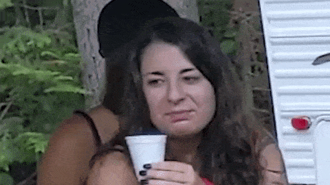a woman is sitting in front of a trailer holding a cup of coffee and making a funny face .