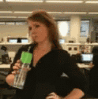 a woman in a black shirt is holding a water bottle with a green lid .