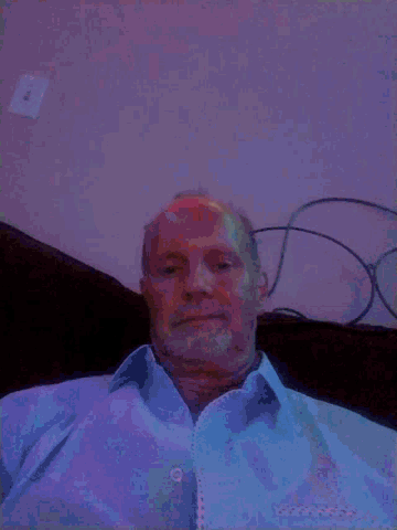 a man with a beard is sitting on a couch with a purple light behind him .
