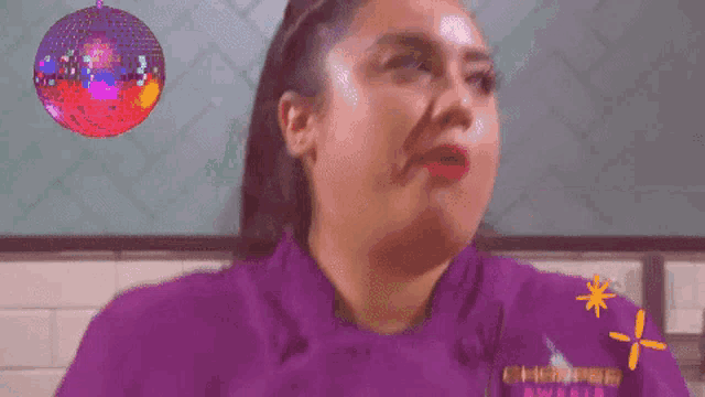 a woman in a purple chef 's coat is crying in front of a disco ball .