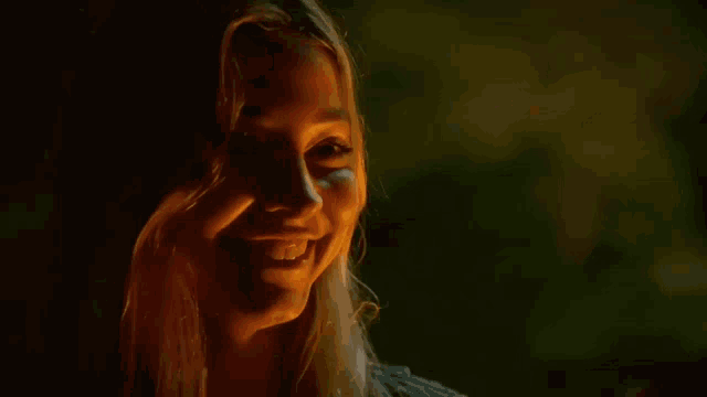 a woman is laughing while holding a bottle of beer in her hand in a dark room .