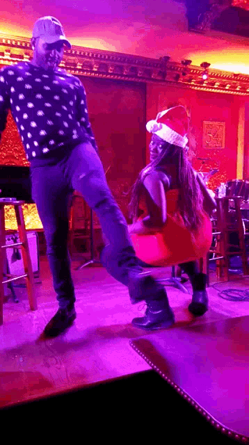 a man wearing a santa hat is kicking a woman in a red dress