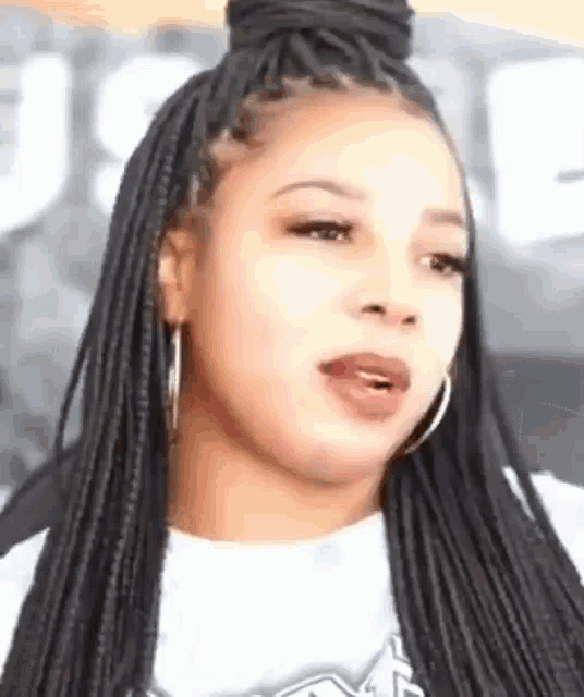 a woman with braids and hoop earrings is wearing a white t-shirt .