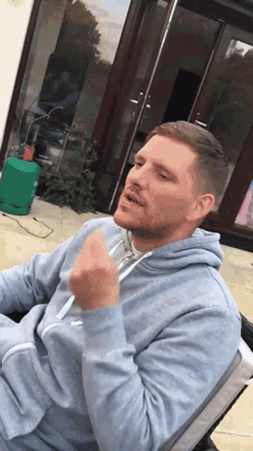 a man in a grey hoodie is sitting in front of a green gas bottle