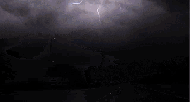 lightning strikes across a dark night sky above a road