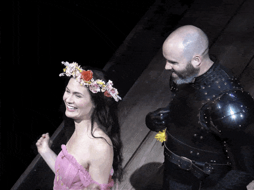 a man in armor stands next to a woman in a pink dress with a flower crown on her head