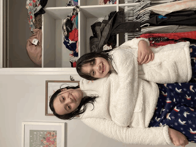 two girls hugging in front of a closet with a framed picture that says merry christmas on it