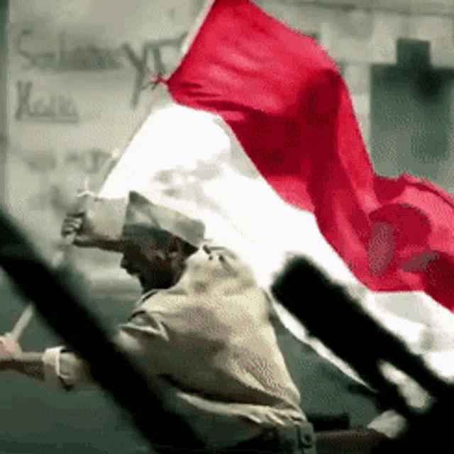 a man is holding a red and white flag in front of a sign that says selamat hari