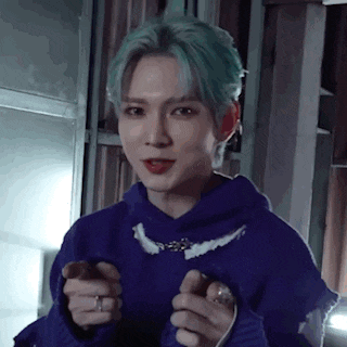 a young man with green hair is wearing a blue hoodie and holding a ring in his hand .