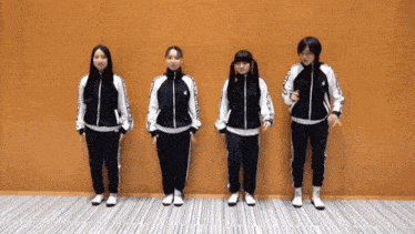 a group of girls are standing in front of a wall wearing black and white jackets with the word asics on them