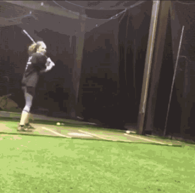 a woman is swinging a baseball bat in a cage .