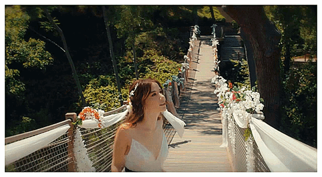 a woman in a white dress is walking across a bridge