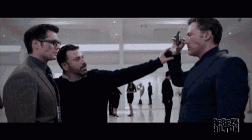 a man in a suit is pointing a gun at another man in a suit and tie