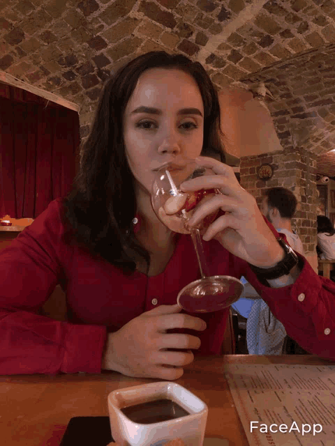 a woman sitting at a table drinking a glass of wine with faceapp on the bottom
