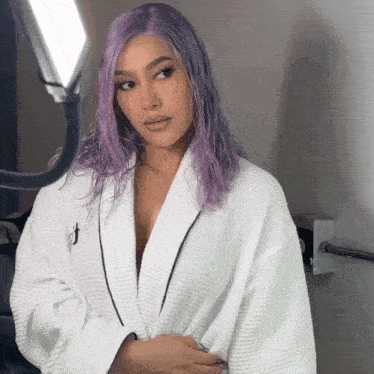 a woman with purple hair is wearing a white robe with the letter j on it