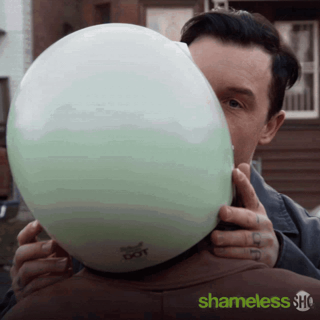 a man holds a helmet over another man 's head with shameless show written on the bottom