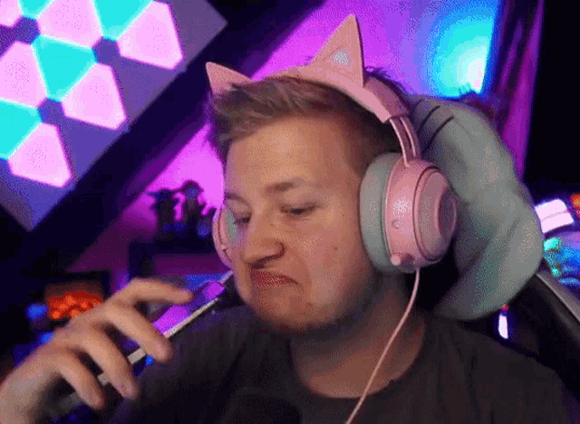 a man wearing a pair of pink cat ears headphones looks at his phone