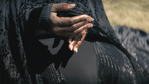 a woman 's hands are crossed over her stomach in a black dress