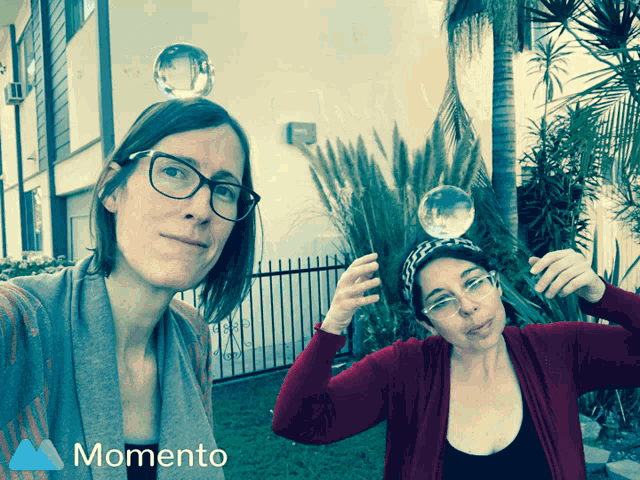 two women are playing with bubbles and a momento logo is behind them