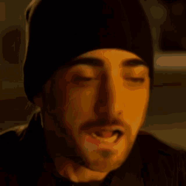 a man with a beard wearing a black hat is making a funny face with his eyes closed .