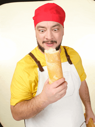 a man wearing a yellow shirt and an apron is holding a loaf of bread