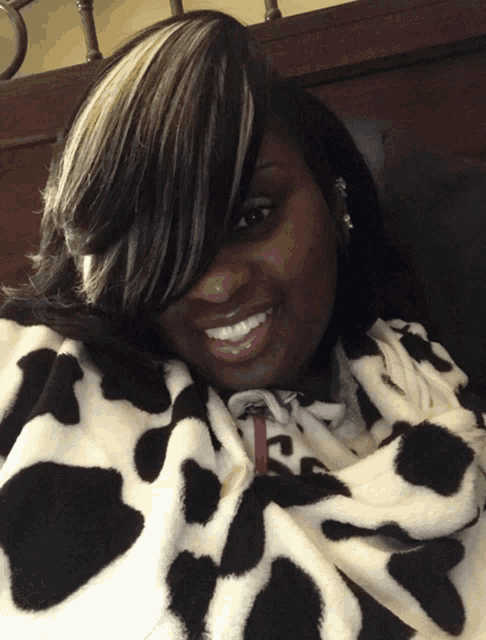 a woman wrapped in a cow print blanket smiles at the camera