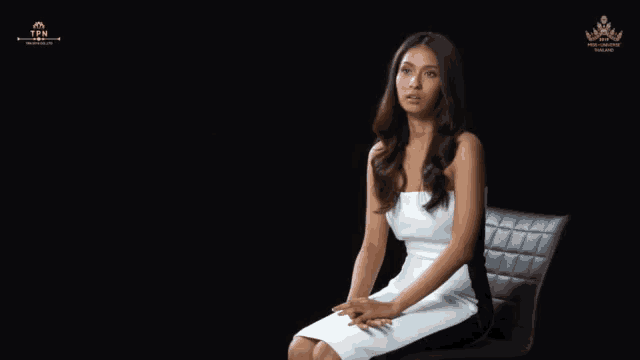 a woman in a white dress sits in a chair in front of a black background that says tfn