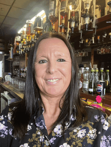 a woman in a floral shirt smiles in front of a bar