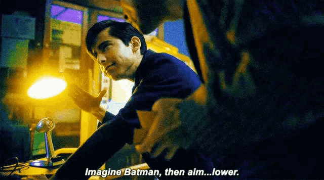a man is talking to another man in a dark room while sitting at a table .