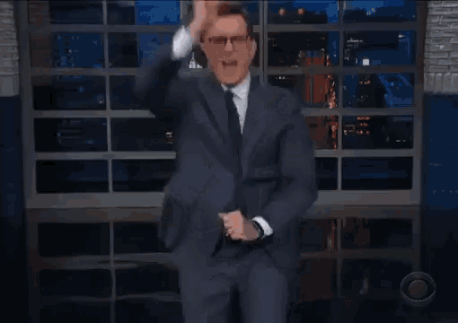 a man in a suit and tie is dancing on a stage in front of a glass wall .