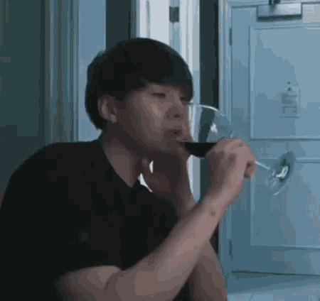 a man in a black shirt is drinking a glass of red wine .