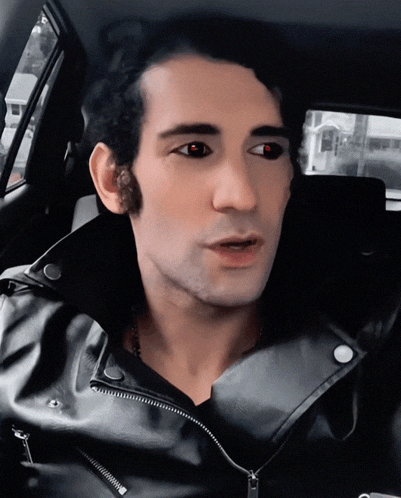 a man in a black leather jacket with red eyes is sitting in a car