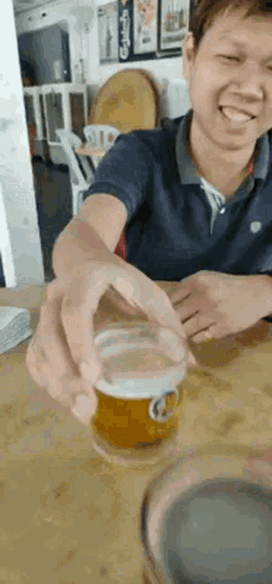 a man is sitting at a table holding a glass of beer in his hand .
