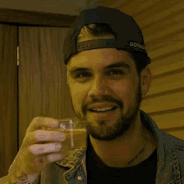 a man wearing a hat that says ' jackeman ' on it drinks from a glass