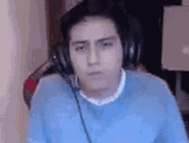 a young man wearing headphones and a blue shirt is looking at the camera .