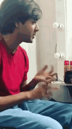 a man in a red shirt is sitting down with his hands outstretched