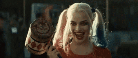 a woman in a harley quinn costume is holding a mallet in her hand and smiling .