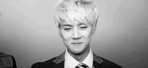 a black and white photo of a young man wearing a suit and tie making a funny face .