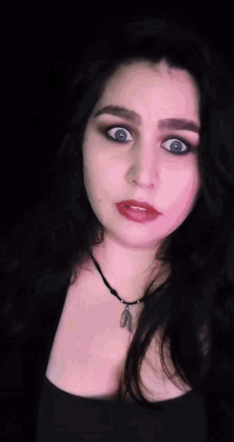 the woman is wearing a black top and a necklace with a feather pendant on it .