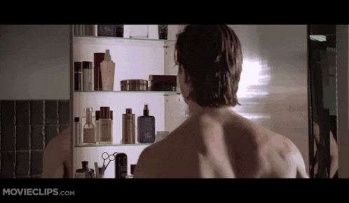 a man looking at his reflection in a mirror with movieclips.com on the bottom left