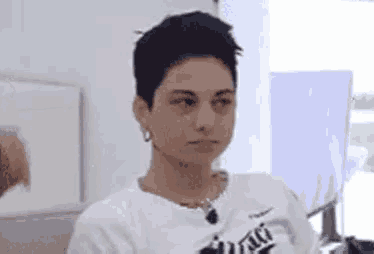 a woman with short black hair is wearing a white sweater and earrings .
