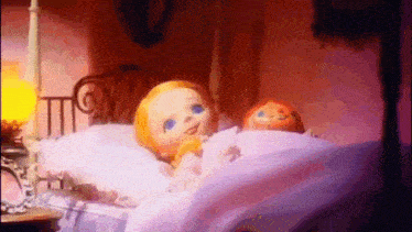 two dolls are laying in a bed in a room