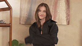 a woman in a black jacket is standing in front of a painting .