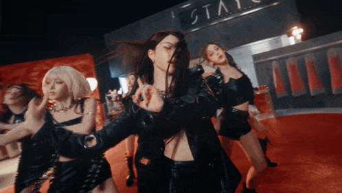 a group of women are dancing in front of a sign that says " stay "