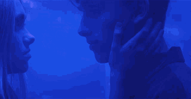 a man and a woman are touching each other 's faces in front of a blue background